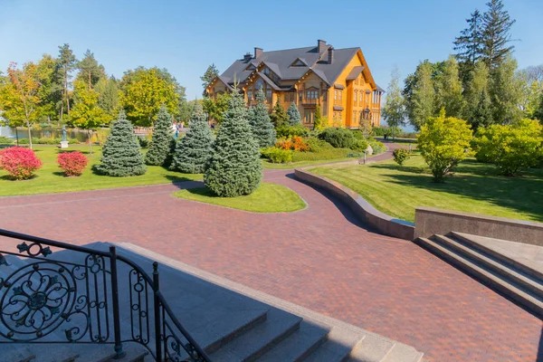 La avenida del parque con pequeños abetos a lo largo de ella, que conduce a una elegante villa de madera — Foto de Stock