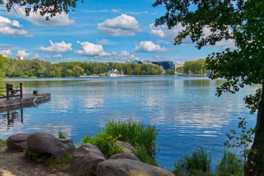 Büyük göl üzerinde yalan büyük taşlarla kıyıdan keyifli bir bakış. Bir mavi gökyüzü ile ele yavaş yavaş yelken Beyaz balya.