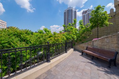 Bir tezgah için rahat bir yerde yeşil ağaçların başında güzel bir şehir manzarası ile yakınındaki bir görüntüleme platformu üzerinde dinlenme duran bulutlar arka planı evler.