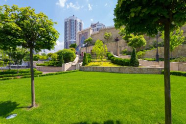 Park süs ve mavi gökyüzü karşı arkasında iki yüksek binalardan duvarla olacak bir yol ile güzel bir yeşil çim.