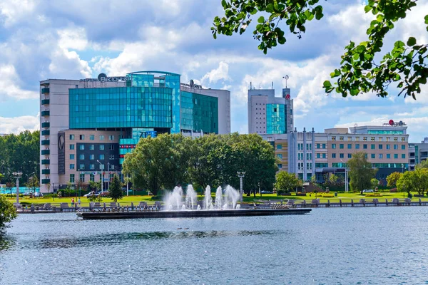 A chic landscape of a pond in the city with beating fountains located on the background of a modern business center building. — Stock Photo, Image