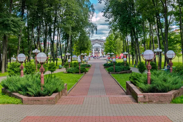 Parque callejón con hermosos macizos de flores verdes decorativos y linternas, que conduce a un enorme edificio — Foto de Stock