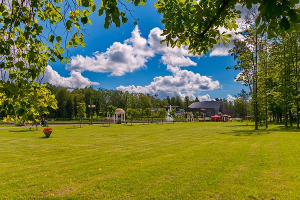 Ein hellgrüner Rasen im Park an einem sonnigen, klaren Tag mit einem überdachten Pavillon in der Ferne, vor einem strahlend blauen Himmel mit weißen Wolken. — Stockfoto