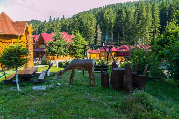 Schöne Komposition auf einem grünen Rasen in Form eines grasenden Hirsches in der Nähe der Schaukelstühle und eines Tisches aus Holz. — Stockfoto