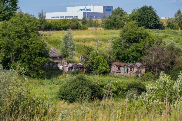 Ruinerna av ett gammalt landsbygdens hus mot bakgrund av en stor fabriksbyggnad — Stockfoto