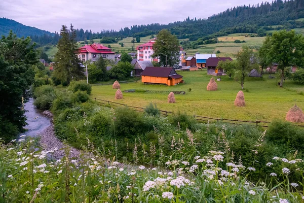 Um pequeno rio na margem de uma aldeia com belas casas em meio a enormes montanhas — Fotografia de Stock