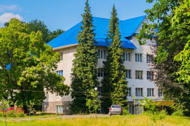 Bej renkli duvarlar ve yeşil park bölgesi arka planı mavi bir çatı ile bina önünde bir araba