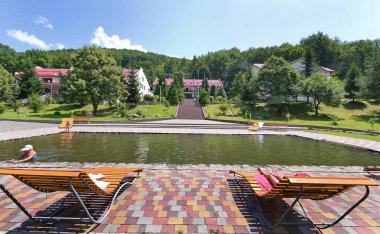 Havuzu kiremitli çatıları ve şezlonglar yakınındaki otel kompleksi yeşil dağların arka planda mavi gökyüzünün altında