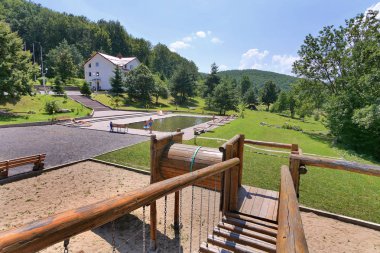 Kürsü Ahşap korkuluk parkta uzaktan ev yeşil çim yakın ve ayakta istirahat insanlarla havuzda güzel manzaralı.