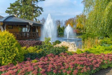 İki çeşme bir yeşil çiçek yatak kırmızı çiçekler ile çevrilidir. Ve bu güzellik küçük bir ev