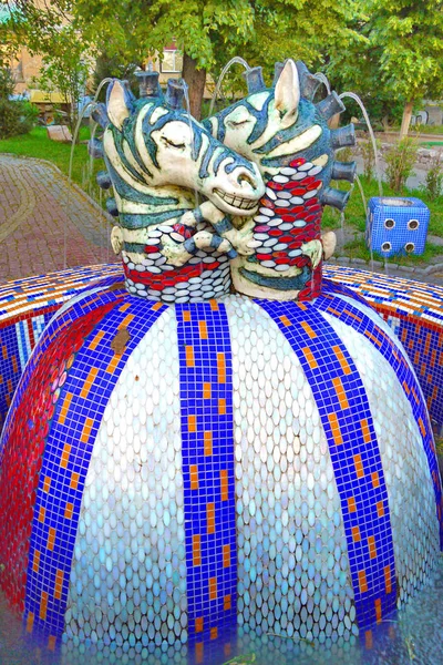Fontana con una grande palla di mosaico in piedi in esso su cui ci sono due teste del cavallo come gli scacchi con fori sulla criniera da cui sgorga acqua in gocciolamenti . — Foto Stock