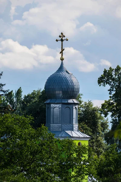 Прекрасний вид на сяючий купол церкви з позолоченим хрестом, що стоїть серед зелених дерев на тлі світлих прозорих хмар на небі . — стокове фото