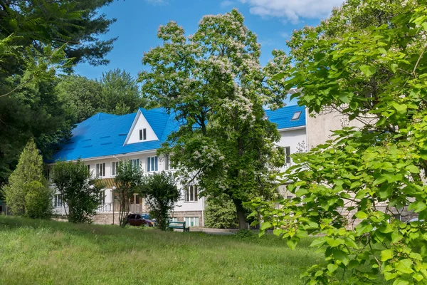 Una casa de vacaciones de pie en una hermosa zona verde entre los árboles con un banco para descansar cerca del césped verde contra el cielo azul . — Foto de Stock
