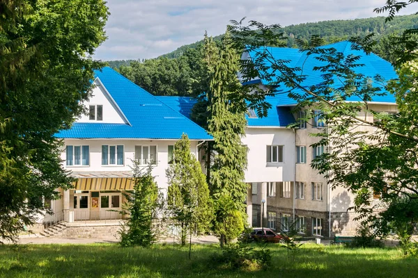 The building is white with a bright blue roof, against a background of green trees