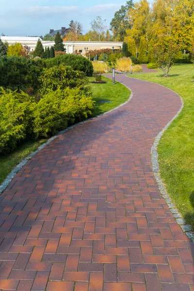 Un sinuoso bulevar con azulejos de dos tonos en el parque. En los lados hay un césped verde con una corta, incluso hierba Fotos De Stock Sin Royalties Gratis