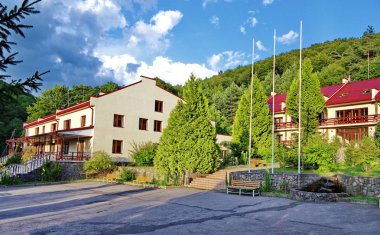 Otel kompleksi ile mavi gökyüzü arka plan üzerinde ormanlık bir dağ eteklerinde, evlerin kırmızı çatılar