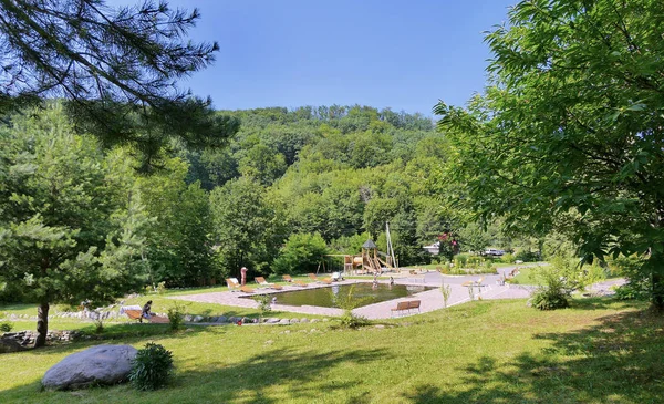 Piscina limpa com bancos de madeira, espreguiçadeiras e um parque infantil no fundo da zona do parque — Fotografia de Stock