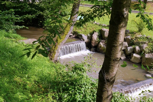 Небольшие водопады проточной воды через бревна в мелкой реке с кучей камней на берегу — стоковое фото