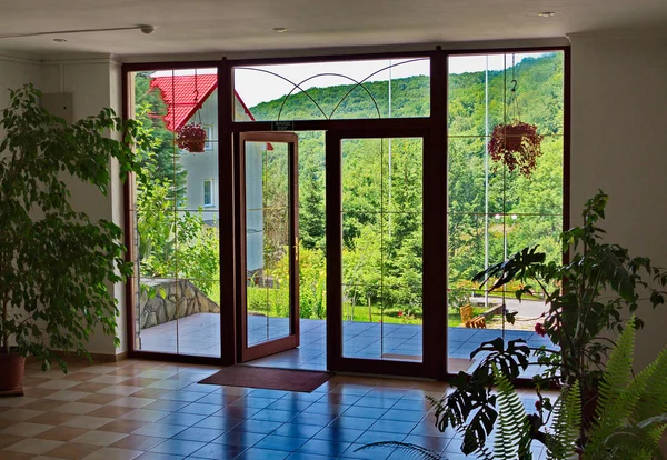 Belle vue depuis le hall du bâtiment sur les pentes luxuriantes des montagnes à travers la porte en bois avec de grandes fenêtres — Photo