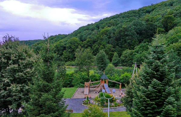 Деревянная игровая площадка на площади возле клумбы на фоне горных панорам — стоковое фото
