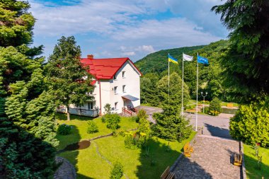 Bayrakları bayrak direkleri ile bulutlar dağ yamaçları üzerinde yüzen mavi gökyüzü karşı modern bir binada yanında durduğunu Rüzgar Rüzgarlar altında çırpınan.