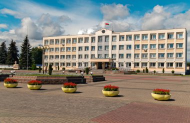 Bir ofis çiçek tencere ile binası önünde büyük bir temiz alanı. Çatıda büyük bulutlar gökyüzünde bir çerçevede ulusal bayrak sallayarak.