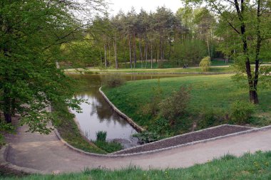Kaldırımları olan yeşil bir parkta gölet. Yürüyen insanlar için bir yer
