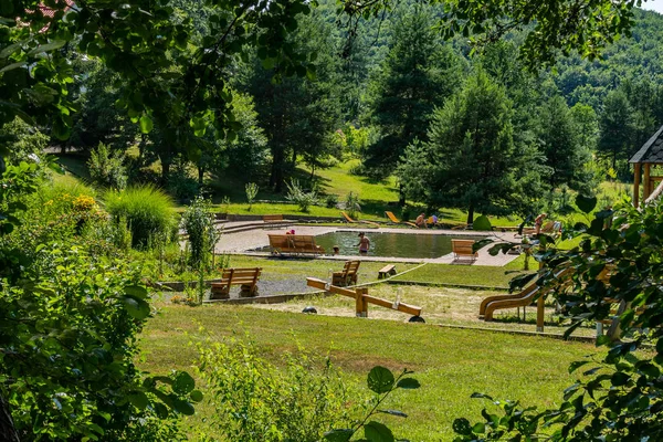 Pool mit Touristen in der Nähe eines Holzspielplatzes vor dem Hintergrund bewaldeter Berge — Stockfoto