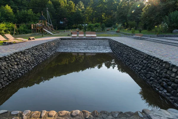 Bequeme Liegestühle in der Nähe eines transparenten Pools, der von einem Stein vor dem Hintergrund eines grünen Waldes angelegt wurde — Stockfoto