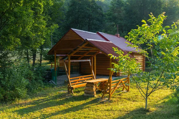 Sauna en una casa hecha de troncos de madera y bancos con una mesa para el descanso de pie bajo un dosel. Todo está situado en medio de la hermosa naturaleza de un bosque verde . — Foto de Stock