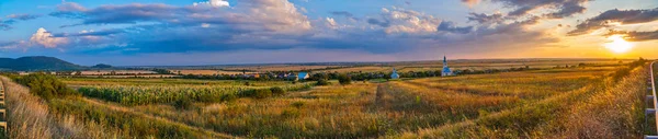 Panorama de um campo perto de uma estrada no fundo de uma aldeia com uma igreja — Fotografia de Stock