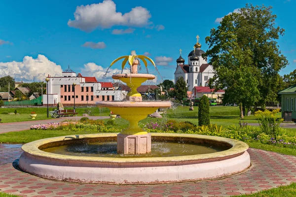 A yellow round fountain sprays water on the square near the flower bed in the city — Stock Photo, Image