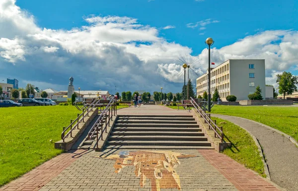 El camino que conduce a las escaleras con una rampa contra la parte posterior del edificio a la derecha y un monumento con un coche estacionado al lado de la izquierda con nubes blancas en el cielo cerró el horizonte . — Foto de Stock