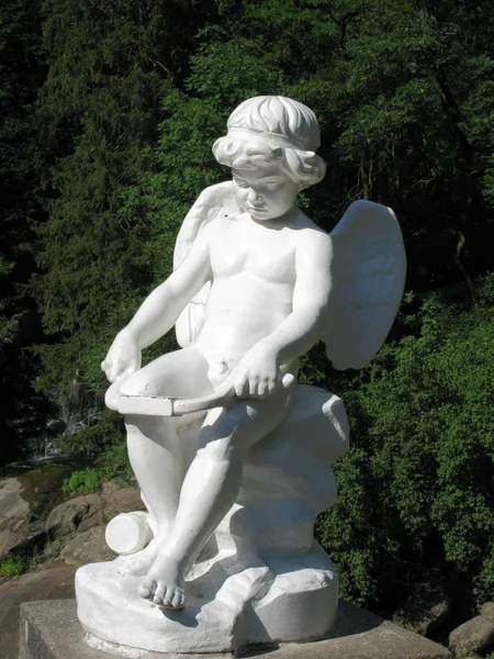 Sculpture en pierre de Cupidon sur fond de feuillus verts — Photo