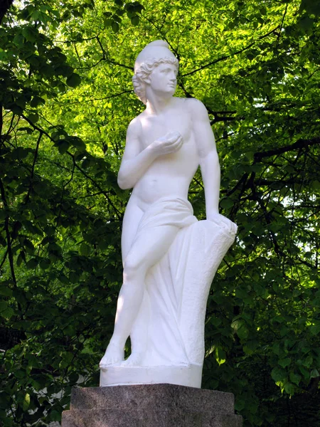 Eine elegante Frauenstatue aus Gips. steht auf einem Sockel inmitten des grünen Baumdickichts. — Stockfoto