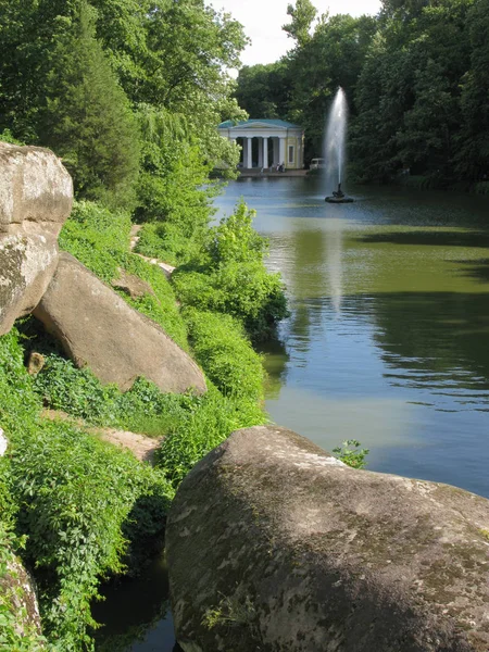 Ein malerischer Blick auf den hoch aufragenden Springbrunnen inmitten eines transparenten Sees vor dem Hintergrund eines wunderschönen architektonischen Gebäudes mit runden Säulen — Stockfoto