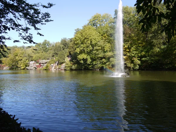 Tourists are resting on the shore of the reservoir with large stones lined on the shore among green trees and a fountain of water pouring in the middle. — Stock Photo, Image