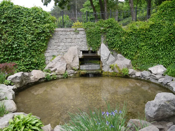Un pequeño estanque redondo rodeado de piedras, con una pequeña cascada — Foto de Stock