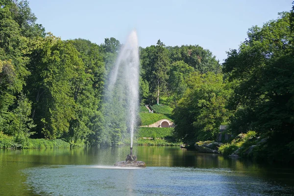 一个大的美丽的装饰喷泉在一个透明的湖泊的背景下的绿色公园区 — 图库照片