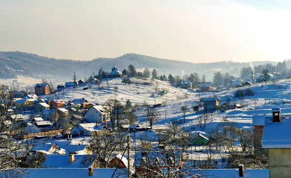 Ländliche Siedlung mit kleinen schneebedeckten Häusern, Höfen und einer Kirche auf einem Hügel — Stockfoto