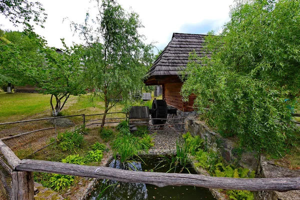En liten brunn med ett hjul under taklägga av ett trähus — Stockfoto