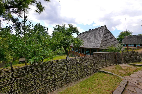 wicker fence and gates enclosing a rural house with a garden