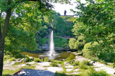 Yüksek deorativny çeşme bir kaide yeşil bir tepenin eteklerindeki gölün ortasındaki