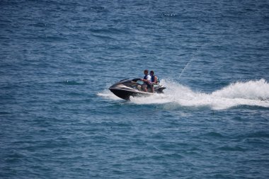 Turistler büyük bir hızla sakin suları denizin ortasında bir su motosiklet binmek. Can yelekleri güvenliği için giyinmiş.