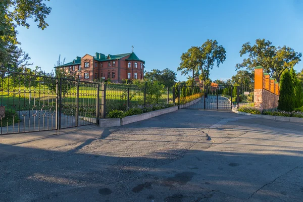 Um parque infantil asfaltado em frente ao portão que leva a uma bela casa de tijolos de dois andares em pé em uma colina com um belo jardim no quintal . — Fotografia de Stock