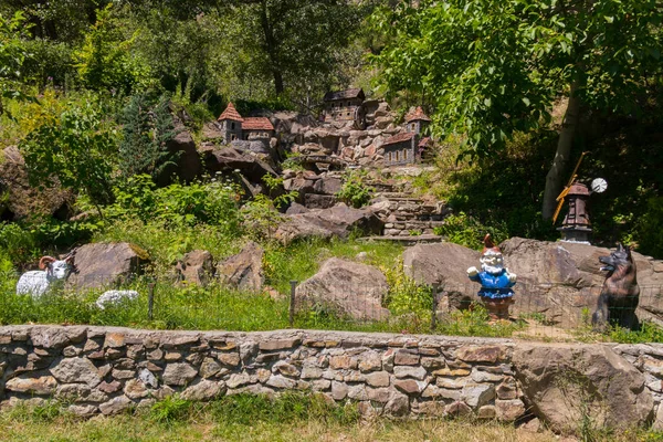 Un modelo de un amargo asentamiento sobre piedras con una estatua de un gnomo de jardín y un perro —  Fotos de Stock