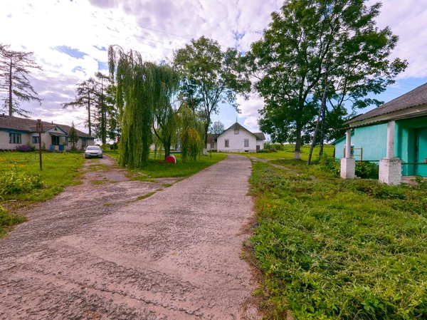 Caminos entre edificios de poca altura en el campo con sauces de cultivo de césped doblando sus ramas al suelo y un coche de pie lado a lado . — Foto de Stock