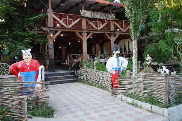 Ingang van het restaurant met helden van nationale sprookjes permanent luisterende in nationale kleren met een rieten hek en een houten kar. — Stockfoto