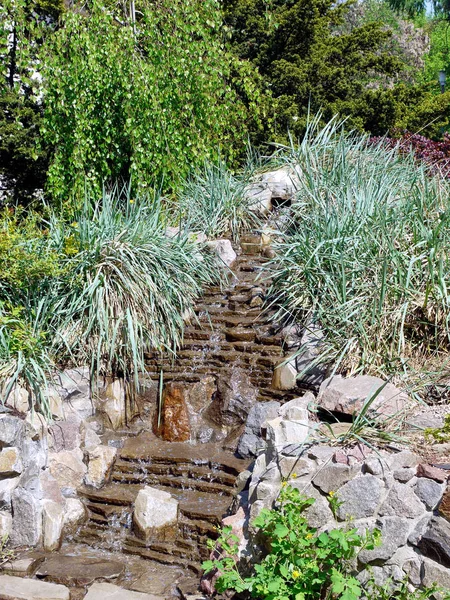 Une belle cascade artificielle sur des pierres plates coule entre les plantations d'herbe ornementale — Photo
