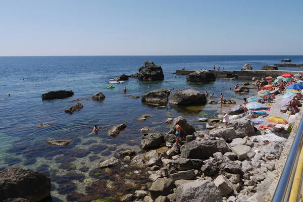 Τουρίστες, στηρίζεται πάνω στην παραλία δίπλα από τις μεγάλες πέτρες πέτρα, πηγαίνει μακριά στη θάλασσα — Φωτογραφία Αρχείου
